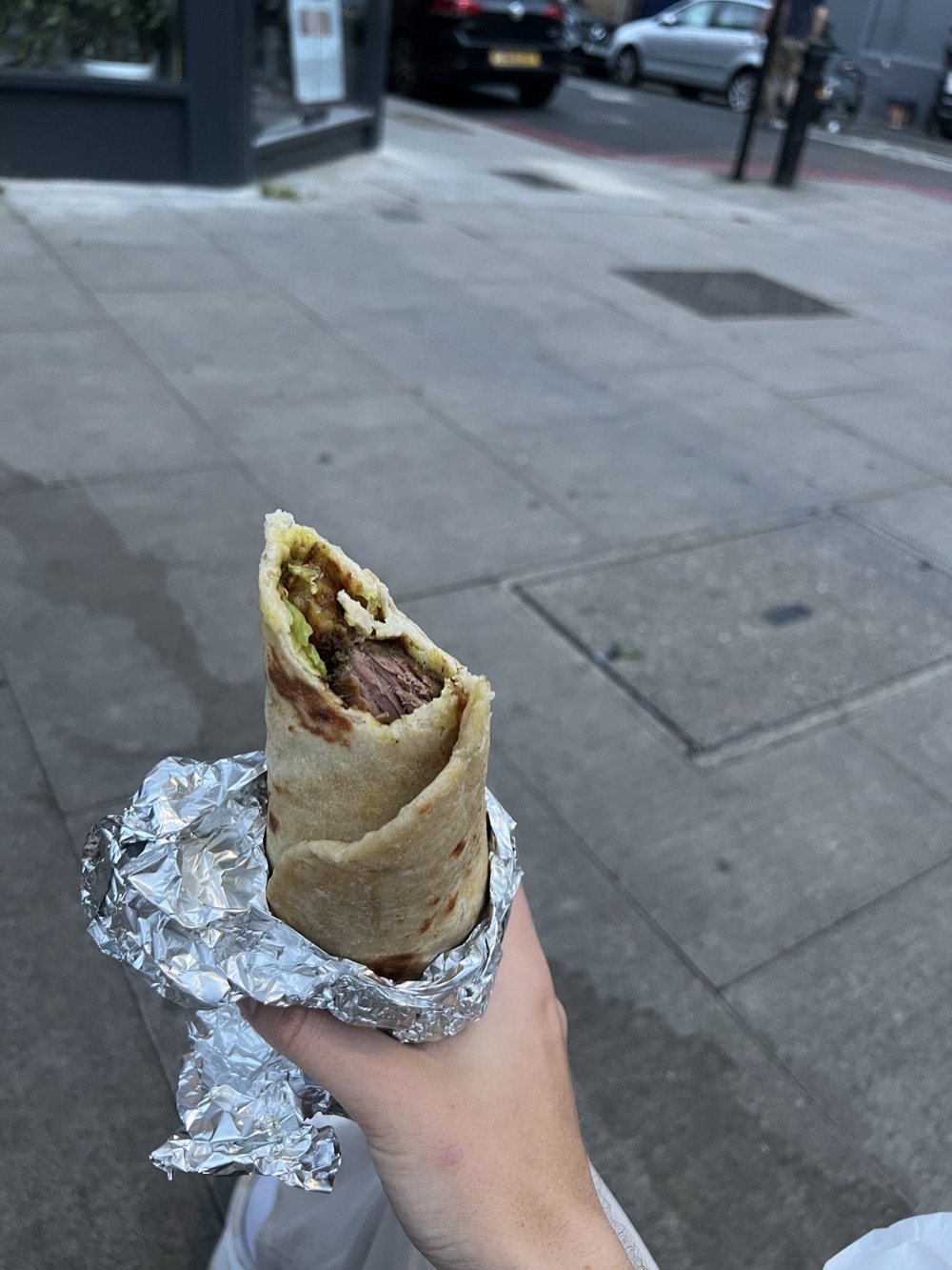 A Caribbean curry wrap in foil, held on Stoke Newington Road
